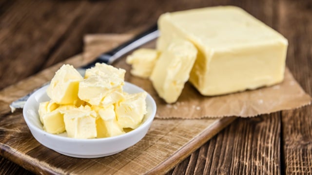 Rectangular block of butter on a white plate with a butter knife beside it.